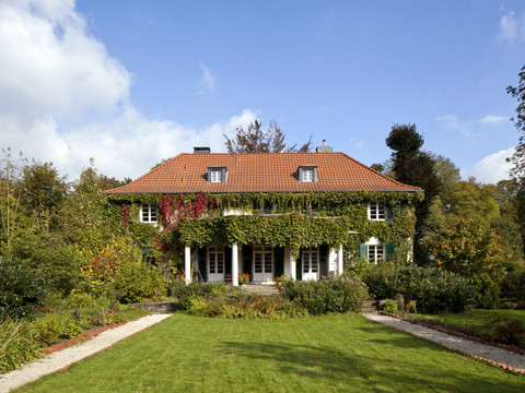 Gutshaus Großes zweistöckiges Landhaus mit rotem Ziegeldach und efeubewachsener Fassade im Grünen.