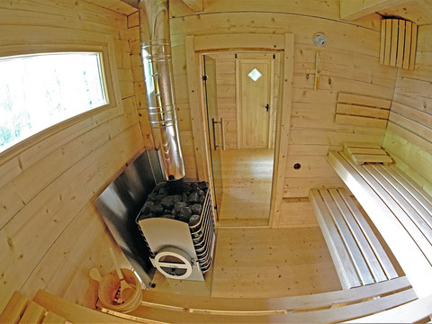 Holzsauna mit Bänken, einem Ofen mit Steinen und einem Eimer mit Kelle; warmes, einladendes Ambiente.