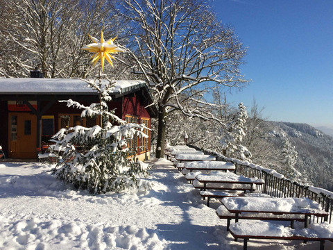 Verschneite Berghütte mit leuchtendem Stern, umgeben von Schneeflocken, Tischen und Bänken.