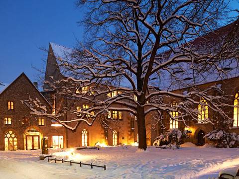 StadtMuseum Pirna im Klosterhof Verschneiter Innenhof bei Dämmerung, beleuchtete Fenster eines historischen Gebäudes, großer Baum im Vordergrund, ruhige Winterstimmung.