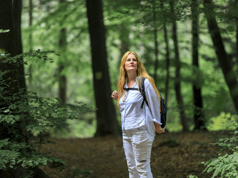 Eine Frau mit Rucksack wandert durch einen dichten, grünen Wald.
