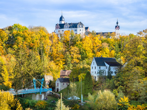 Schloss Rochsburg im Herbst - Schlösser der Leipzig Region Im unteren Bereich des Bildes stehen vereinzelte Häuser und eine Brücke umgeben von einem bunten Laubwald, darüber thront das Schloss Rochsburg, Ausflugsziel, Leipzig Region, Museum
