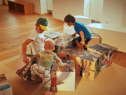 Museum Kinder spielen in einem Museum auf großen Würfeln mit aufgedruckten Stadtbildern.
