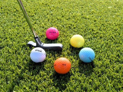 Adventure-Golf am Markkleeberger See - Freizeit in Leipzig und Region Bunte Golfbälle liegen auf dem grünen Gras, daneben steht ein Golfschläger für das Adventure-Golfspiel am Markkleeberger See, Freizeitaktivität, Familienausflug