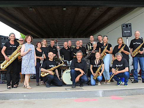 Eine Gruppe von Musikern posiert mit verschiedenen Instrumenten auf einer überdachten Bühne.