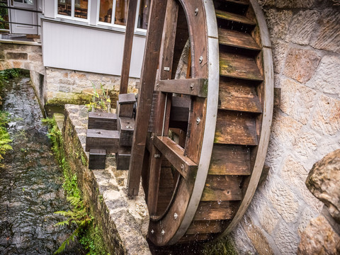 Wasserrad aus Holz an einem kleinen Bachlauf, umgeben von Natursteinmauern und Pflanzen.Wooden water wheel on a small stream, surrounded by natural stone walls and plants.Dřevěné vodní kolo u malého potoka, obklopené přírodními kamennými zídkami a rostlinami.Drewniane koło wodne przy małym strumieniu, otoczone naturalnymi kamiennymi ścianami i roślinami.Houten waterrad bij een beekje, omringd door natuurstenen muren en planten.Ruota idraulica in legno presso un piccolo ruscello, circondata da muri in pietra naturale e piante.