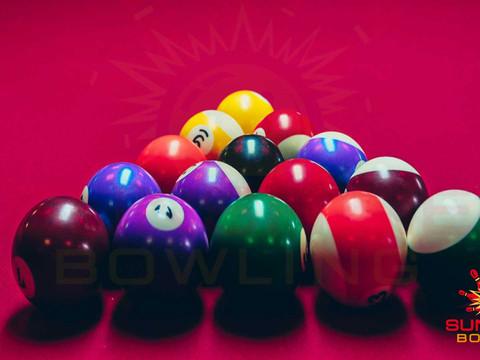 Kleurrijke bowlingballen liggen op een rode tafel, met het logo van Sunshine Bowling op de achtergrond.