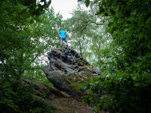 Felsgruppe unterhalb der Kaiserkrone Eine Person in blauem T-Shirt und Shorts steht auf einem großen, moosbedeckten Felsen, umgeben von dichtem, grünem Wald.