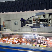 Allräucherei Prahm-Theke-Apen.jpg Ein Verkäufer in weißem Kittel grüßt freundlich hinter einer gut bestückten Fischtheke.