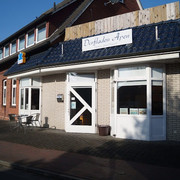 Dorfladen-Apen_Apen_2022.jpg Dorfladen in Apen mit roten Backsteinwänden, weißem Eingang und Sitzgelegenheiten im Freien.