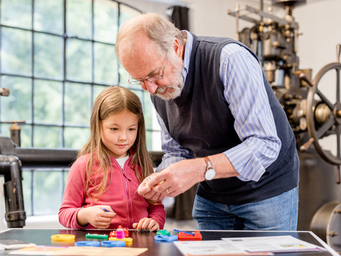 Spürnasen-Rallye Ein älterer Mann zeigt einem neugierigen Mädchen Modelle in einem industriellen Museumsumfeld.