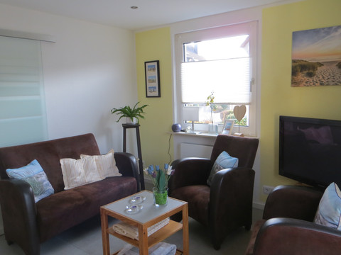 IMG_3851.JPG Gemütliches Wohnzimmer mit braunen Sesseln, Sofas, kleinem Tisch, Pflanzen und einem Bild an gelber Wand.