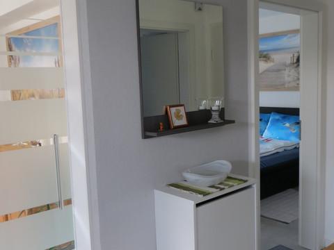 IMG_3859.JPG Moderner Flur mit weißem Schuhschrank, Spiegel und Blick in ein helles Wohnzimmer im Hintergrund.