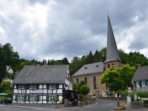 Ensemble Volberg <p>Historisches Fachwerkhaus neben einer alten Kirche mit spitzem Turm unter bewölktem Himmel.</p>