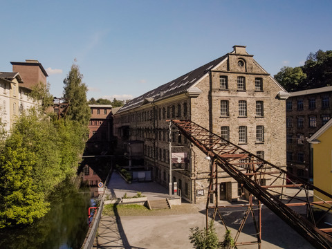 Wülfingmuseum Alte Fabrikgebäude aus Backstein am Fluss mit bläulichem Himmel und grüner Umgebung bei Sonnenschein.