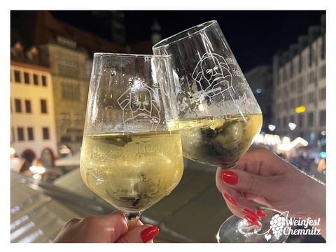 Twee champagneglazen proosten in een nachtelijke stadssfeer op het wijnfestival van Chemnitz.