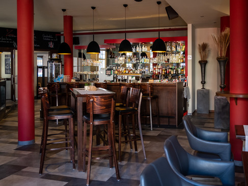 Ein stilvoll eingerichtetes Restaurant mit hohen, roten Säulen, Holzmöbeln und einer beleuchteten Bar.