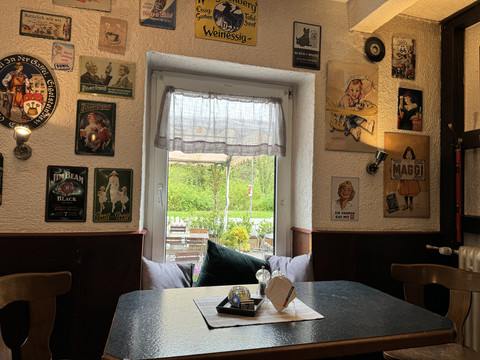 Zur Quelle der Strunde - Innenansicht Gemütliche Gaststube mit rustikaler Einrichtung, Postern an den Wänden und Blick auf grüne Terrasse.