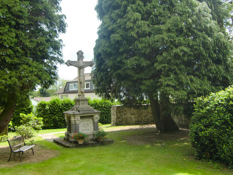 Gedenkkreuz Kreuzdenkmal aus Stein in einem grünen, parkähnlichen Garten, umgeben von hohen Bäumen.