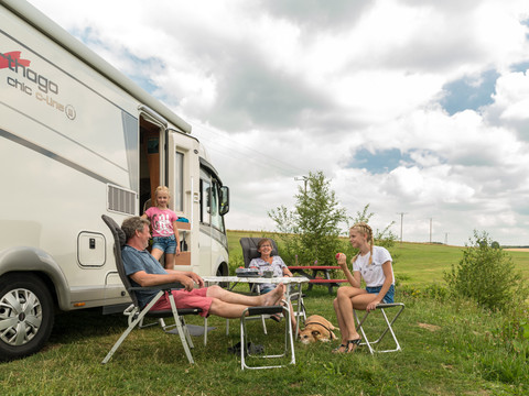 Campingpark im Bergischen Land Familie entspannt bei einem Wohnmobil auf einer Wiese unter bewölktem Himmel. Ländliche Umgebung.
