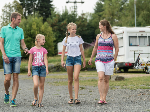 Campingpark im Bergischen Land Eine Familie spaziert fröhlich auf einem Campingplatz, im Hintergrund steht ein Wohnwagen.
