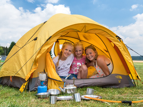 Campingpark im Bergischen Land <p>Drei fröhliche Kinder in einem gelben Zelt auf einer Wiese, umgeben von Campingausrüstung.</p>