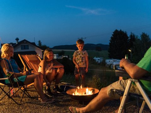 Campingpark im Bergischen Land <p>Familie genießt bei Dämmerung am Campingplatz ein Lagerfeuer, umgeben von ländlicher Idylle.</p>