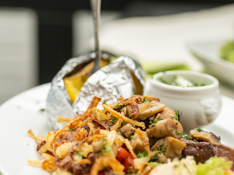 Landhotel Napoleon Kartoffel in Alufolie mit Pilzpfanne und Kräuterbutter auf weißem Teller, im Hintergrund Petersilie.