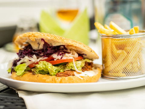Landhotel Napoleon Pulled-Pork-Burger mit Salat, Rotkohl und Tomaten, serviert mit Pommes frites im Metallkörbchen.