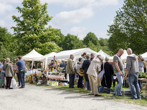 "Jrön un Jedön" Menschen schlendern über einen lebhaften Outdoor-Markt mit weißen Zelten und grüner Vegetation.