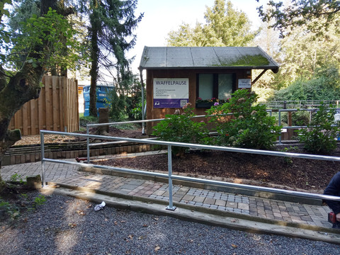 Waffelpause Ein Holzpavillon mit Schild "WAFFELPAUSE" umgeben von Pflanzen und gepflastertem Gehweg.