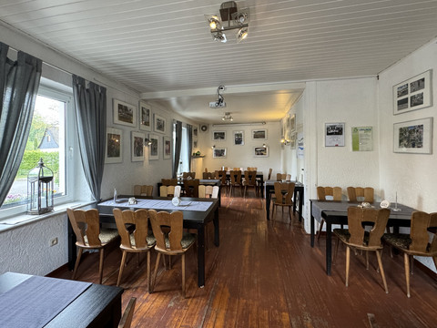 Zur Quelle der Strunde - Innenansicht <p>Gemütliches Restaurant mit Holzböden, Fensterblick und Tischen, umgeben von gerahmten Bildern.</p>