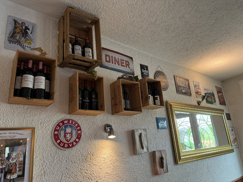 Zur Quelle der Strunde - Ansicht Wanddekoration Weinregale aus Holzkisten an einer Wand, dekoriert mit nostalgischen Schildern und einem Spiegel.