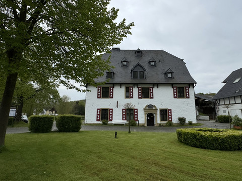 Außenansicht Ein zweigeschossiges, historisches Gebäude mit weißer Fassade und roten Fensterläden.