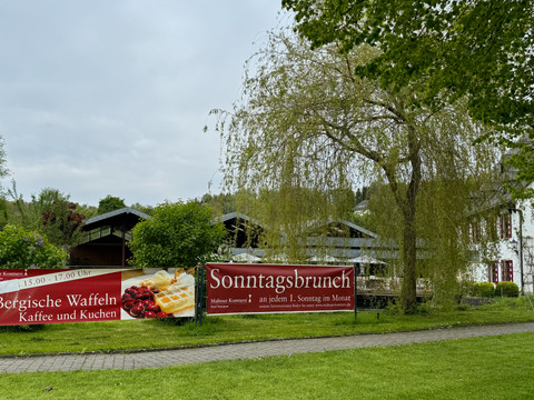 Banner - Bergische Waffeln Traditionelle Waffel- und Brunch-Werbung vor einem Gasthof, umgeben von grüner Landschaft.