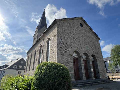 ev. Kirche Rückansicht St. Martinus Kirche in Wiehl, historisches Steingebäude mit spitzem Turm vor blauem Himmel.