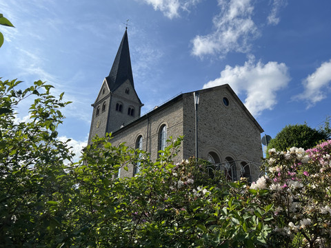evangelische Kirche <p>Kirche mit hohem Turm und blühenden Büschen im Vordergrund, blauer Himmel im Hintergrund.</p>