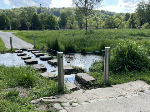 Furt im Wiehlpark <p>Stufen aus Naturstein überqueren einen klaren Bach inmitten einer grünen, bewaldeten Landschaft.</p>