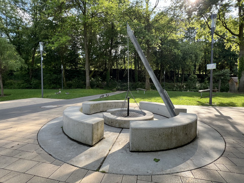 frei zugänglicher Grillplatz im Wiehlpark <p>Moderne Sonnenuhr aus Metall und Betonbänken in einem grünen Park bei Sonnenschein.</p>