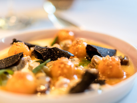 Hotel Zur Post Leckere Gourmetkomposition mit Trüffelscheiben, Melonenkugeln und feinen Kräutern in eleganter Anrichtung.