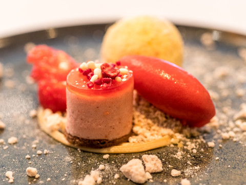 Hotel Zur Post Fruchtig dekoriertes Dessert auf dunklem Teller: Rote Mousse, Sorbet, goldene Kugel und Krümeldeko.