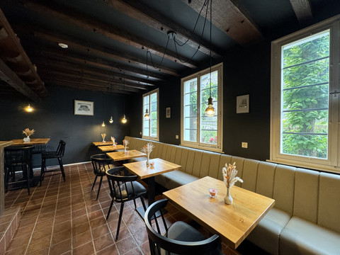 Zum Haus Olpe - Ansicht Innenbereich  Gemütlicher Café-Raum mit Holztischen, modernen Stühlen und gedämpfter Beleuchtung, ideal zum Entspannen.