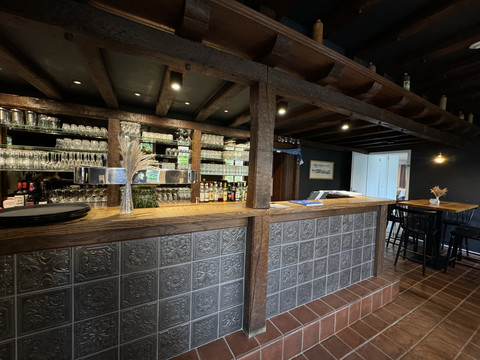 Zum Haus Olpe - Ansicht Bar Gemütliche Bar mit rustikalem Holztresen, Fliesendetails und Regalen voller Gläser unter warmem Licht.