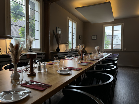 Zum Haus Olpe - Innenansicht  Ein langer Holztisch in einem stilvoll eingerichteten Restaurant, gedeckt mit roten Servietten und Gläsern.