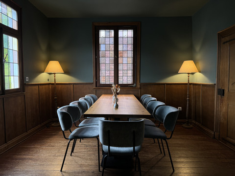 Zum Haus Olpe - Innenansicht separater Raum  Ein eleganter Konferenzraum mit Holzwänden, einem großen Tisch, acht Stühlen und zwei Stehlampen.