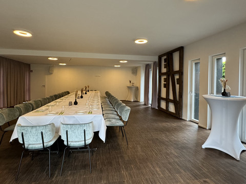 Zum Haus Olpe - Innenansicht Veranstaltungsraum Langer, eleganter Konferenzraum mit gedecktem Tisch, Holzfußboden und modernen Lichtinstallationen.