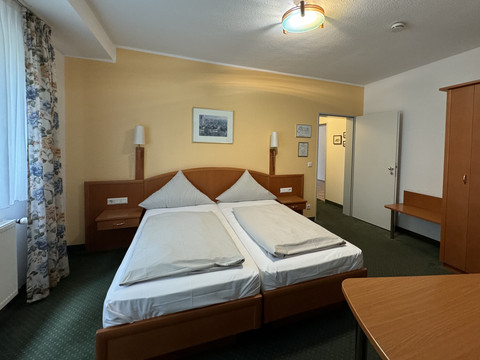 Hotel Garni Alt Refrath - Doppelzimmer 1 Gemütliches Hotelzimmer mit zwei Einzelbetten, Holzmöbeln, hellem Teppichboden und Fenster mit Vorhängen.