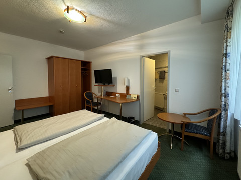 Hotel Garni Alt Refrath - Doppelzimmer 1  Ein gemütliches Hotelzimmer mit Doppelbett, Schreibtisch, Wandfernseher und offenem Zugang zum Bad.