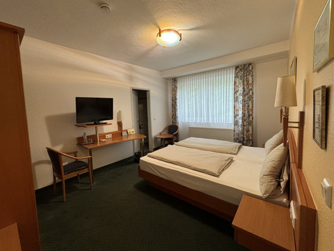 Hotel Garni Alt Refrath - Doppelzimmer 1  Ein gemütliches Hotelzimmer mit Doppelbett, Flachbild-TV, Schreibtisch und großem Fenster mit Vorhang.