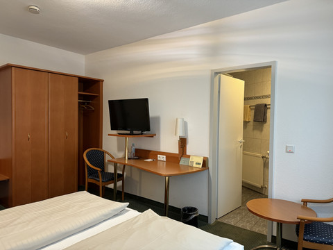 Hotel Garni Alt Refrath - Doppelzimmer 1  Fernseher und Kleiderschrank in modernem Hotelzimmer mit offenem Bad; heller, einladender Raum.